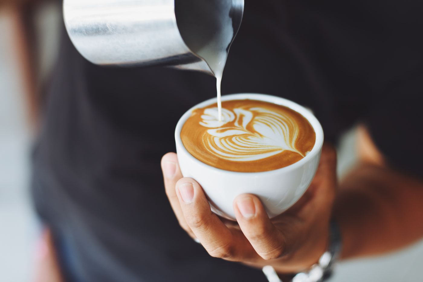 A barista pouring a drink behind the counter of a busy shop.